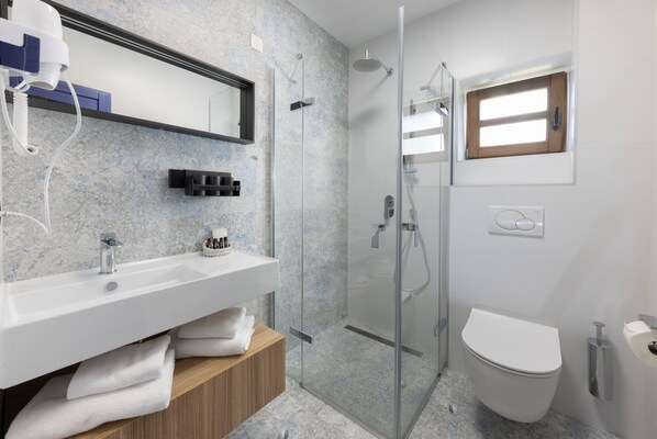 Un baño moderno con ducha de vidrio, lavamanos blanco sobre tocador de madera y un inodoro.