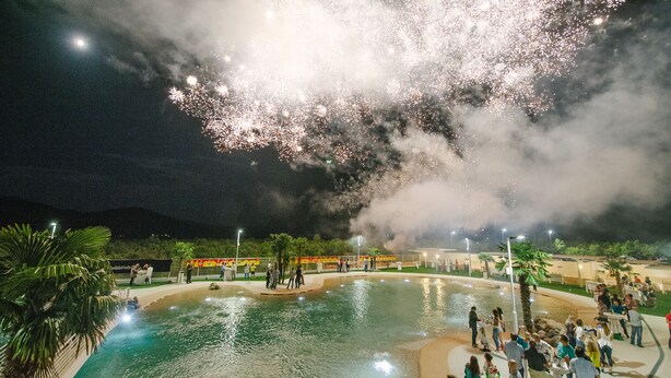 A pool area with people around it, surrounded by a landscaped garden.