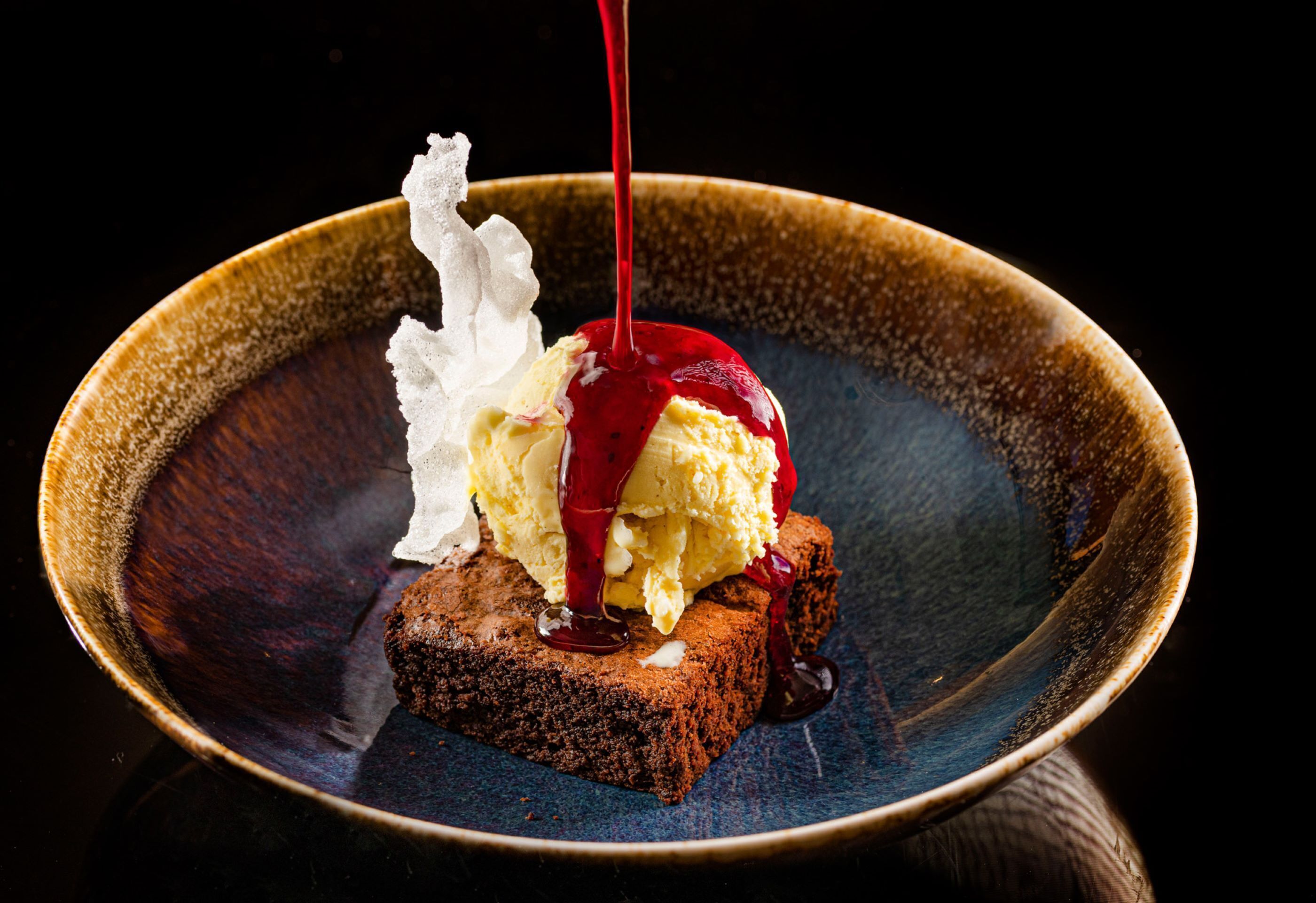 Dessert mit Eiscreme und Sirup in einer Keramiktasse auf einem Kuchenstück.