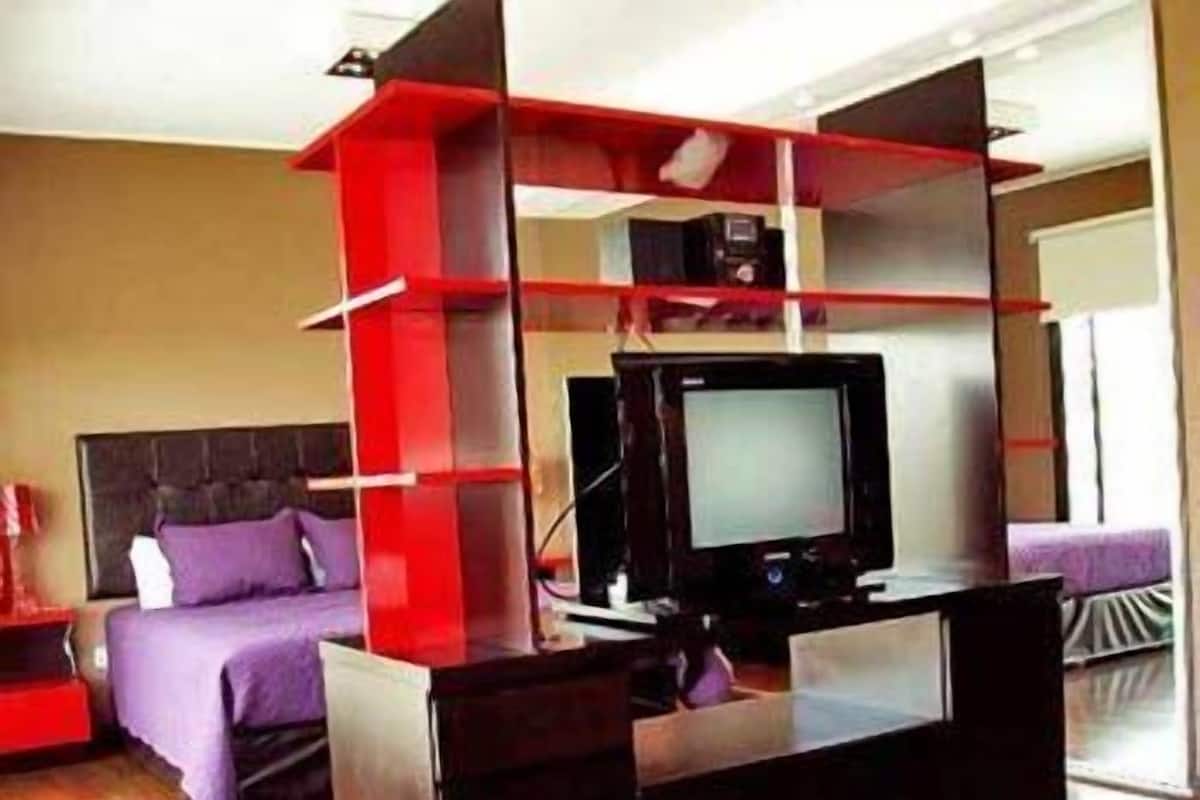 A modern hotel room with a bed, a TV, and a desk with a computer.