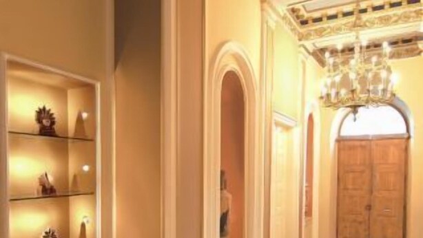 A hallway with a wooden floor, a chandelier, and a door with a wooden panel.