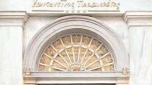 A double wooden door with intricate carvings, set in a classical architectural style with a stone frame and an arched window above.
