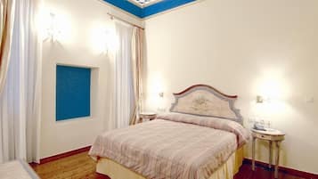 A bedroom with a bed, two bedside tables, a nightstand, a window with curtains, and a blue accent wall.