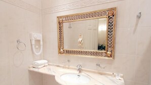 A bathroom with a beige tiled wall, a white sink with a gold-framed mirror above it, and a towel rack to the left.
