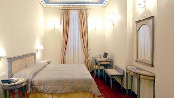Habitación de hotel con cama, mesitas de noche, escritorio, silla, espejo y ventana con cortinas.