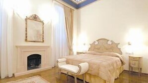 A bedroom with a bed, a chair, a fireplace, and two bedside tables.