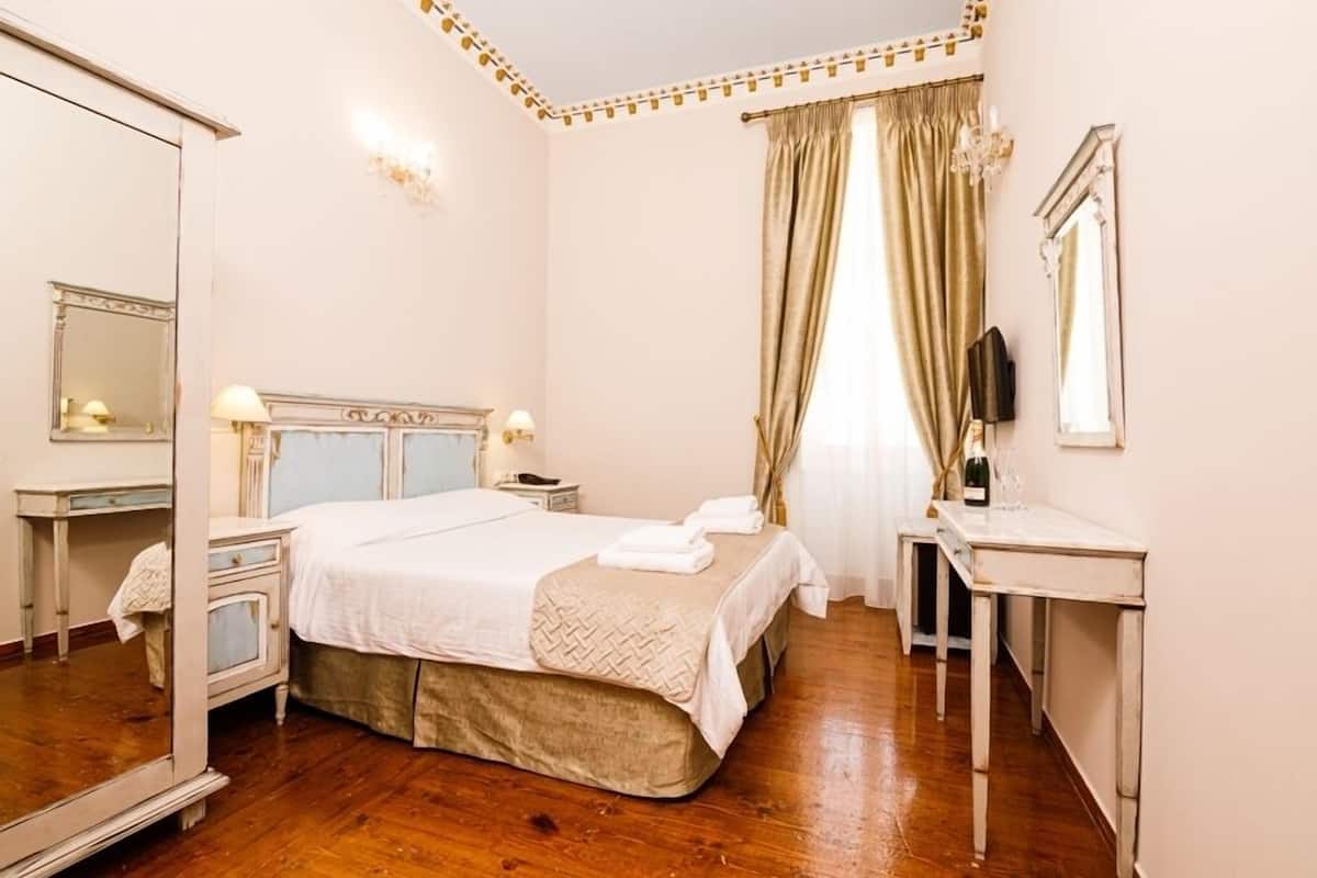 Hotellihuone, jossa on suuri sänky, yöpöytä, peili ja työpöytä tuolilla.