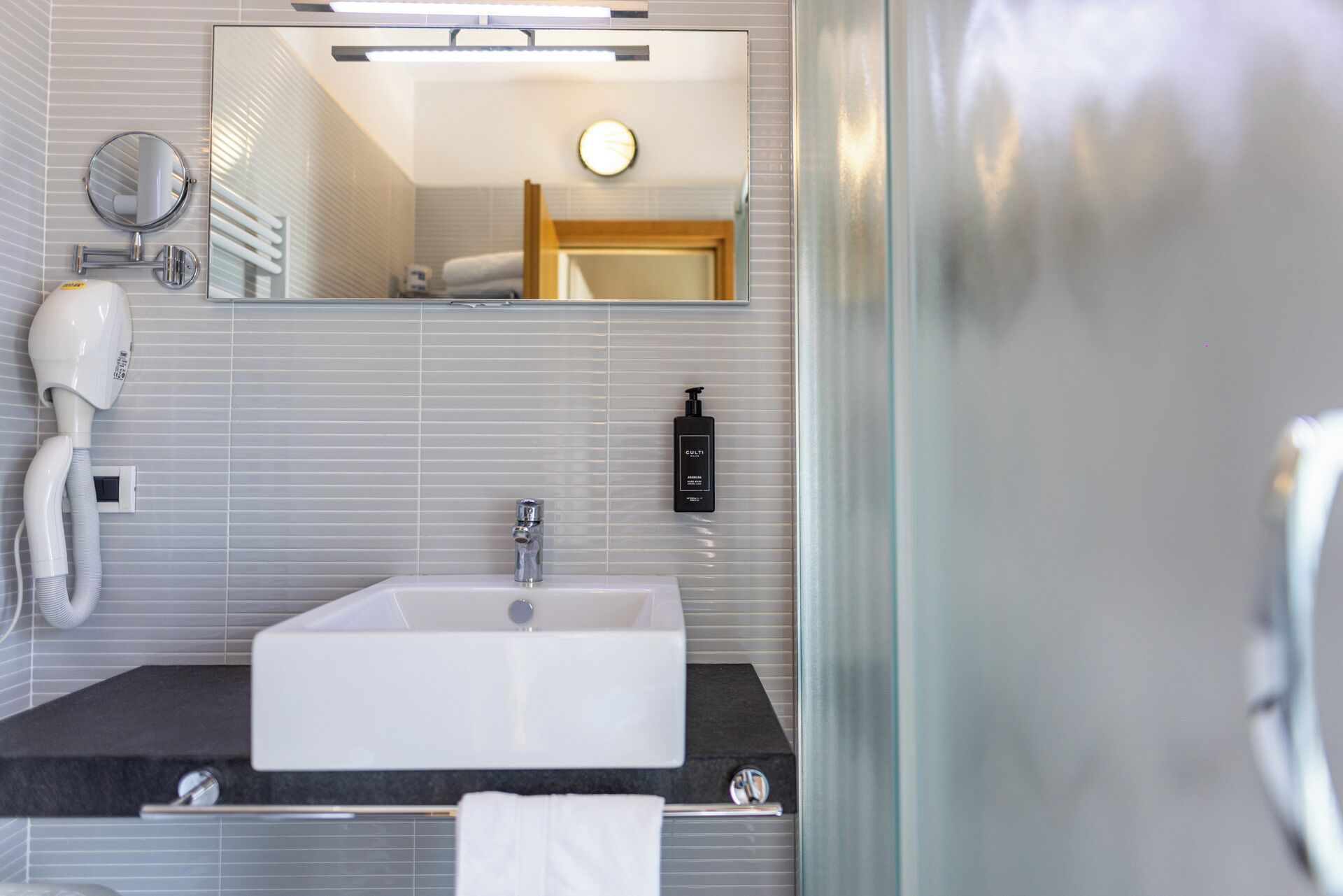 Un baño moderno con un lavabo rectangular, un espejo, un secador de pelo y una botella de champú.