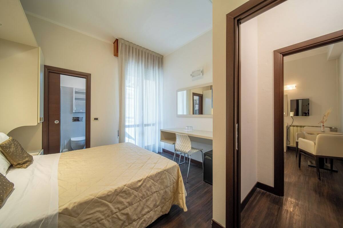 A hotel room with a bed, a desk, a chair, a mirror, and a bathroom.