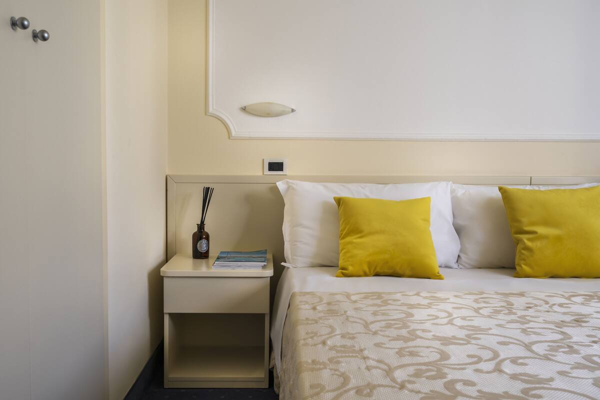 A hotel room with a bed, nightstand, and a wall-mounted light fixture.