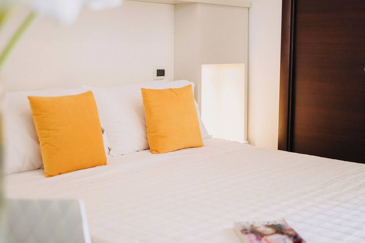 A hotel room with a bed, two pillows, a bedside table, and a magazine on the bed.