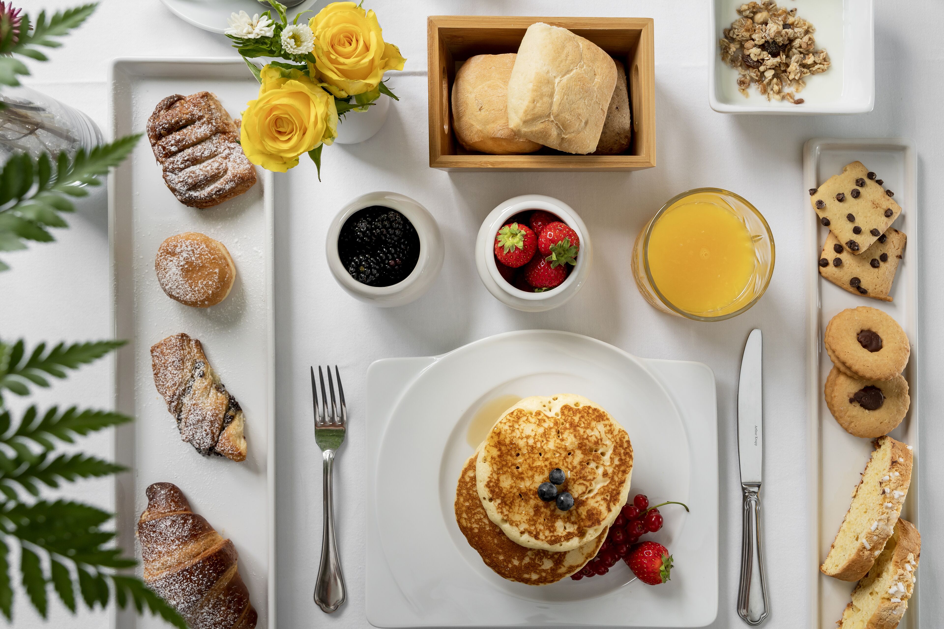 A breakfast setting with pastries, fruits, and beverages on a white table.