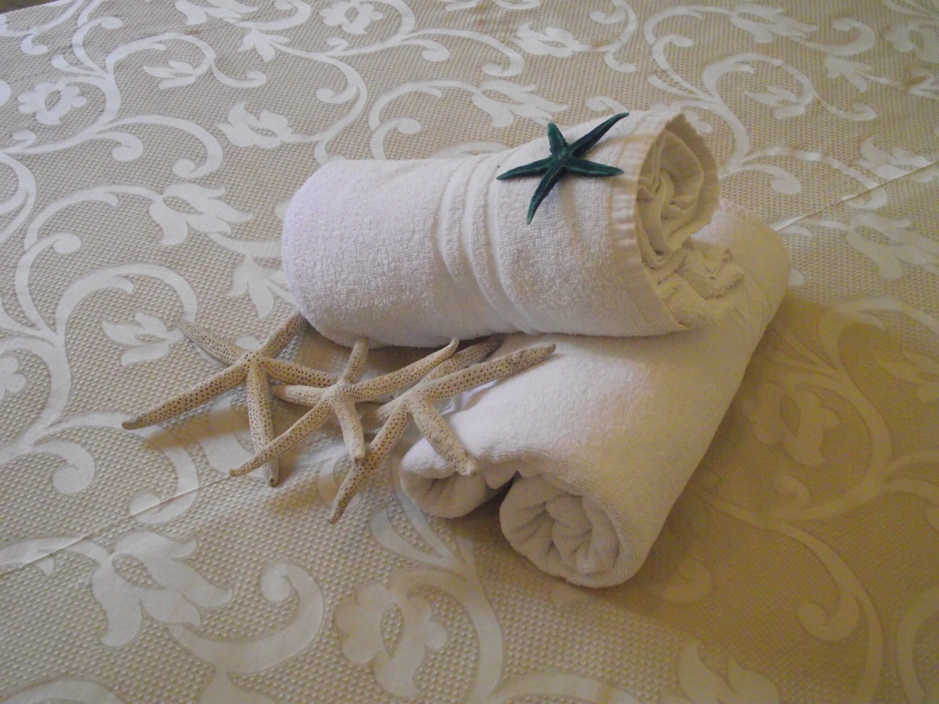 A rolled white towel with a starfish on a patterned fabric surface.