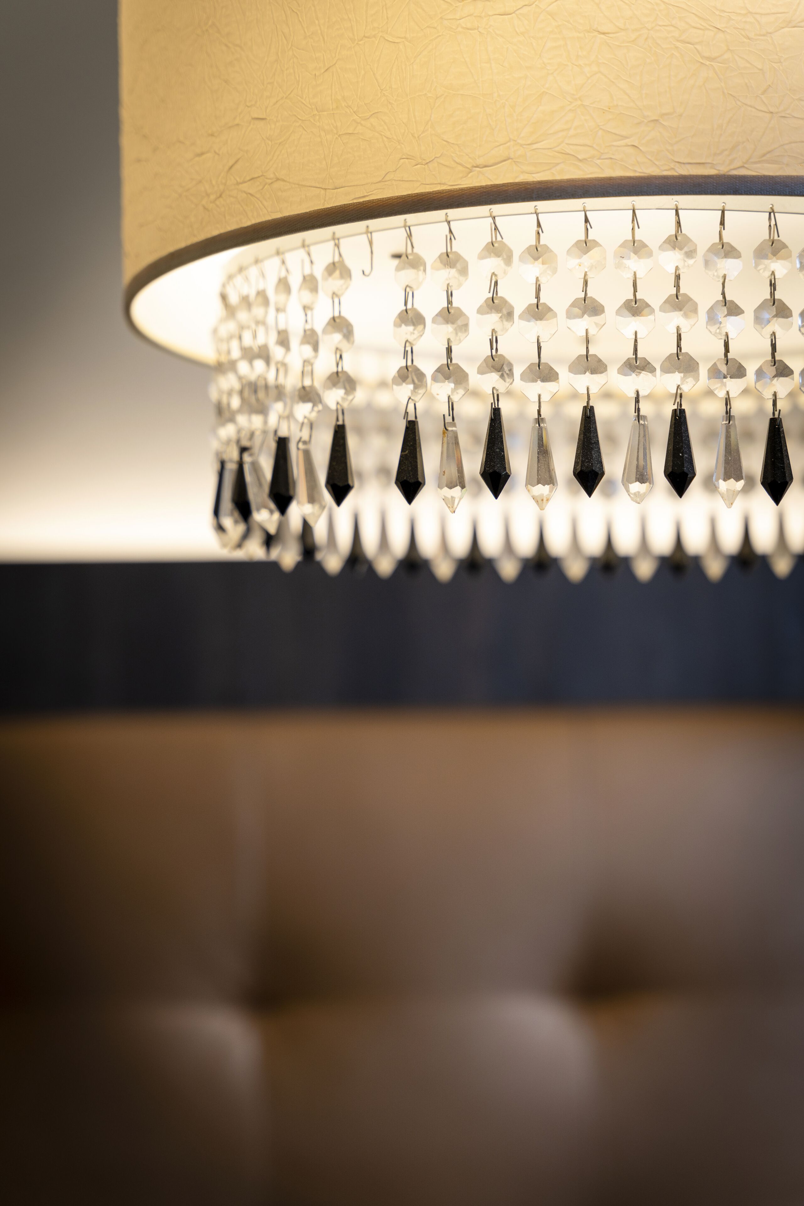 A chandelier with multiple crystal elements and a lighted base, set against a textured wall.