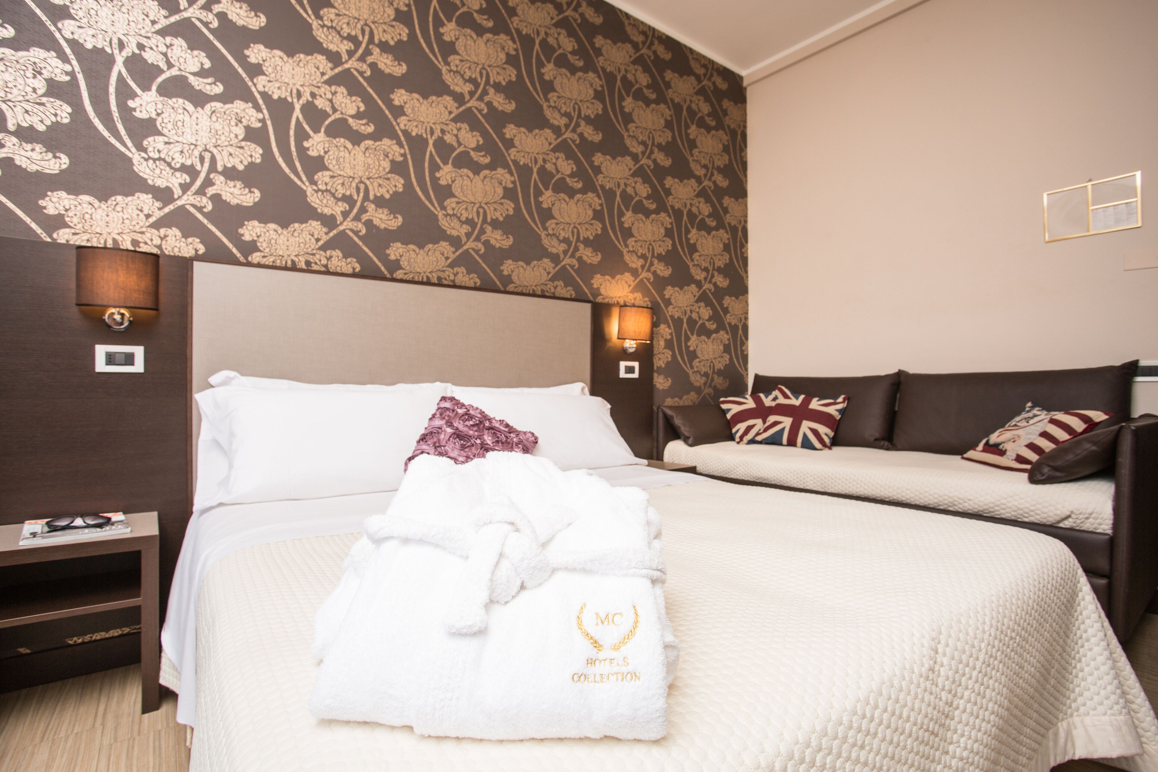 A hotel room with two beds, a nightstand, and a wall with a floral pattern.