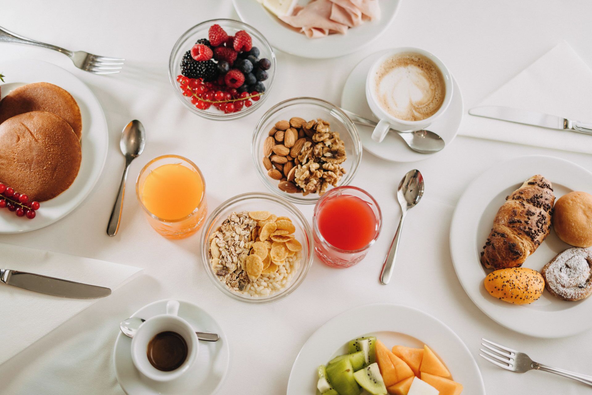 Desayuno con tortitas, bayas, nueces, cereales, jugo de naranja, jugo de frutos rojos, café y pasteles.