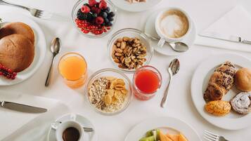 Desayuno con tortitas, bayas, nueces, cereales, jugo de naranja, jugo de frutos rojos, café y pasteles.