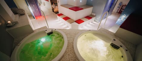 Two hot tubs with different colored water, a seating area with red cushions, and a modern interior design.
