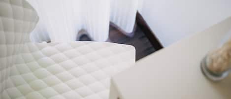 Una habitación con una butaca blanca acolchada y una mesa blanca con un objeto de vidrio encima.