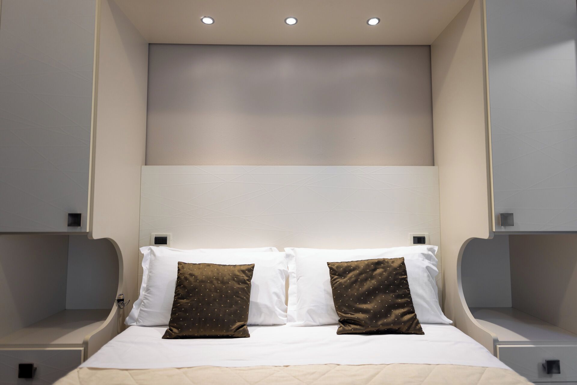 A modern hotel room with a large bed, two pillows, and a headboard with integrated lighting.