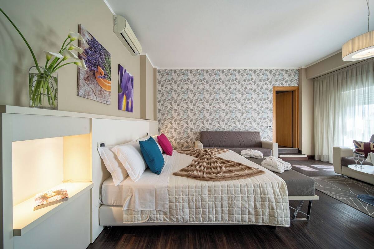 A modern hotel room with a large bed, a sofa, and a desk area.