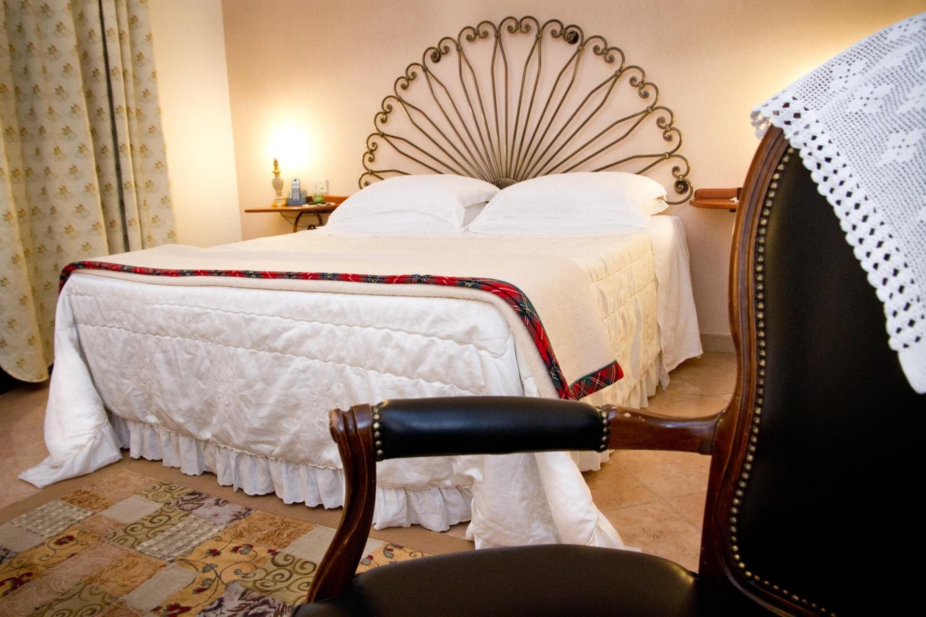 A neatly made bed with a decorative headboard, a wooden chair with a cushion, and a patterned rug on the floor.