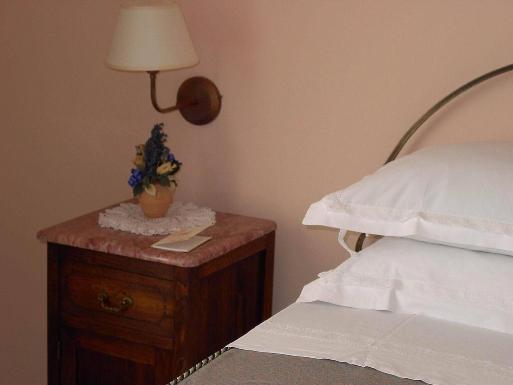 A bed with white linens, a bedside table with a lamp, and a small potted plant.