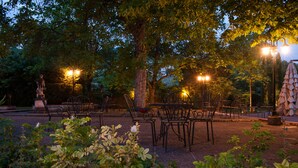 An outdoor seating area with tables and chairs, surrounded by trees and illuminated by street lamps. - La Primula (Potenza)