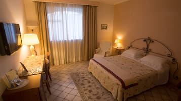A hotel room with a bed, a desk with a lamp, a chair, and a television.