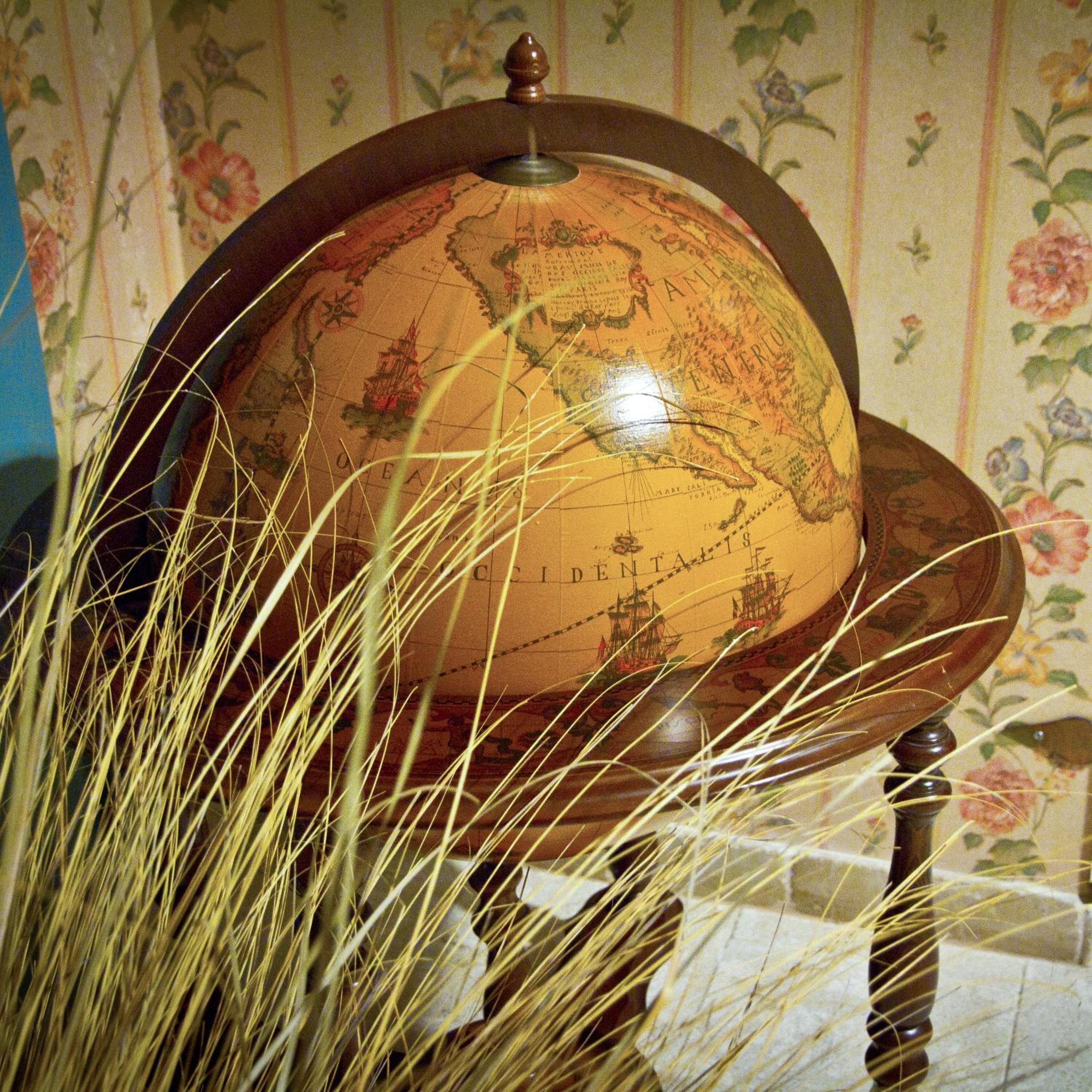 Un globe terrestre posé sur un socle en bois, avec un papier peint à motifs floraux en arrière-plan.