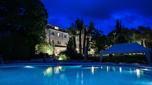 A swimming pool with a large building in the background, surrounded by trees and a covered area. - La Primula (Potenza)