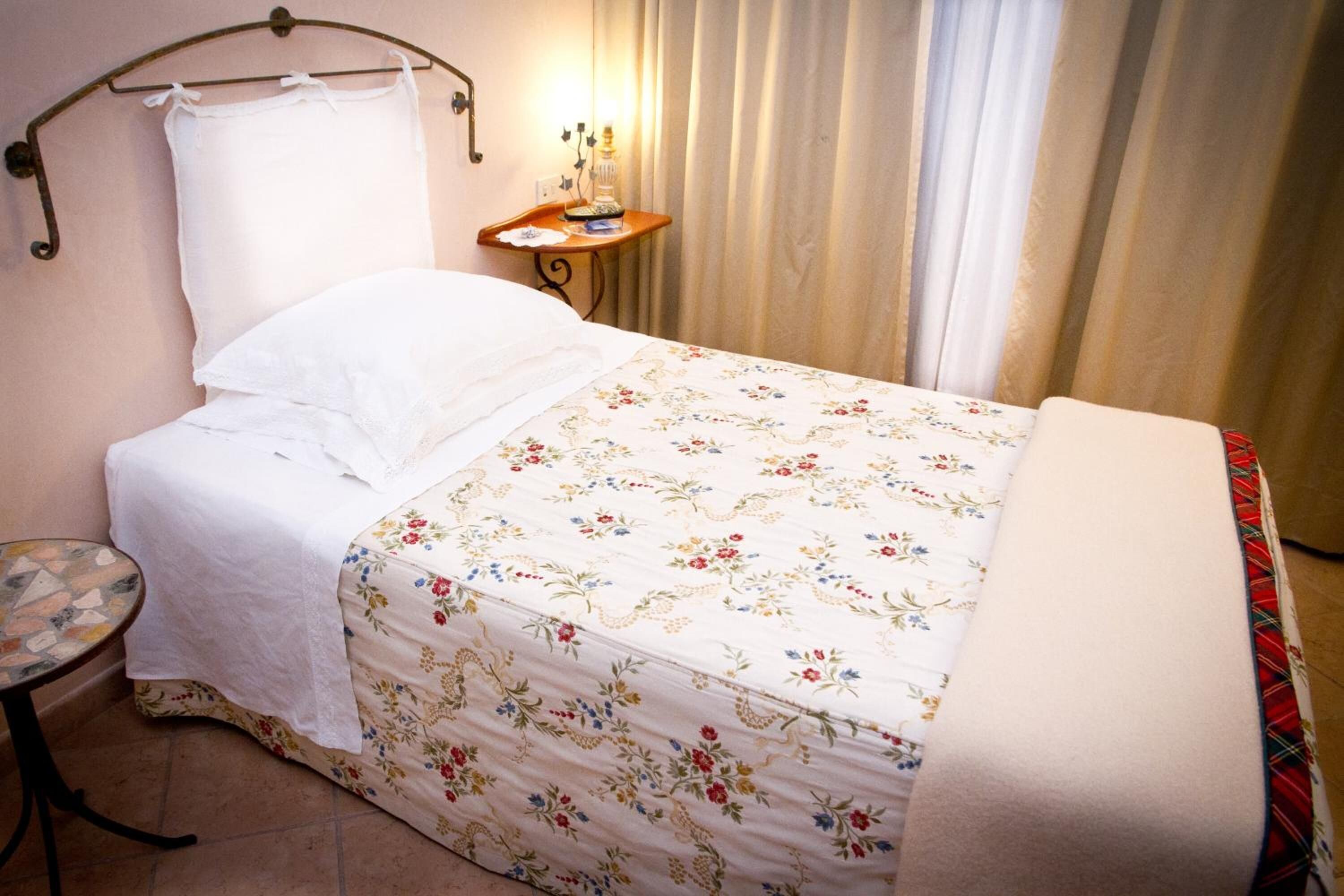 Un lit bien fait, recouvert d’une couvre-lit à motifs floraux, une table de chevet avec une lampe et une petite table ronde.