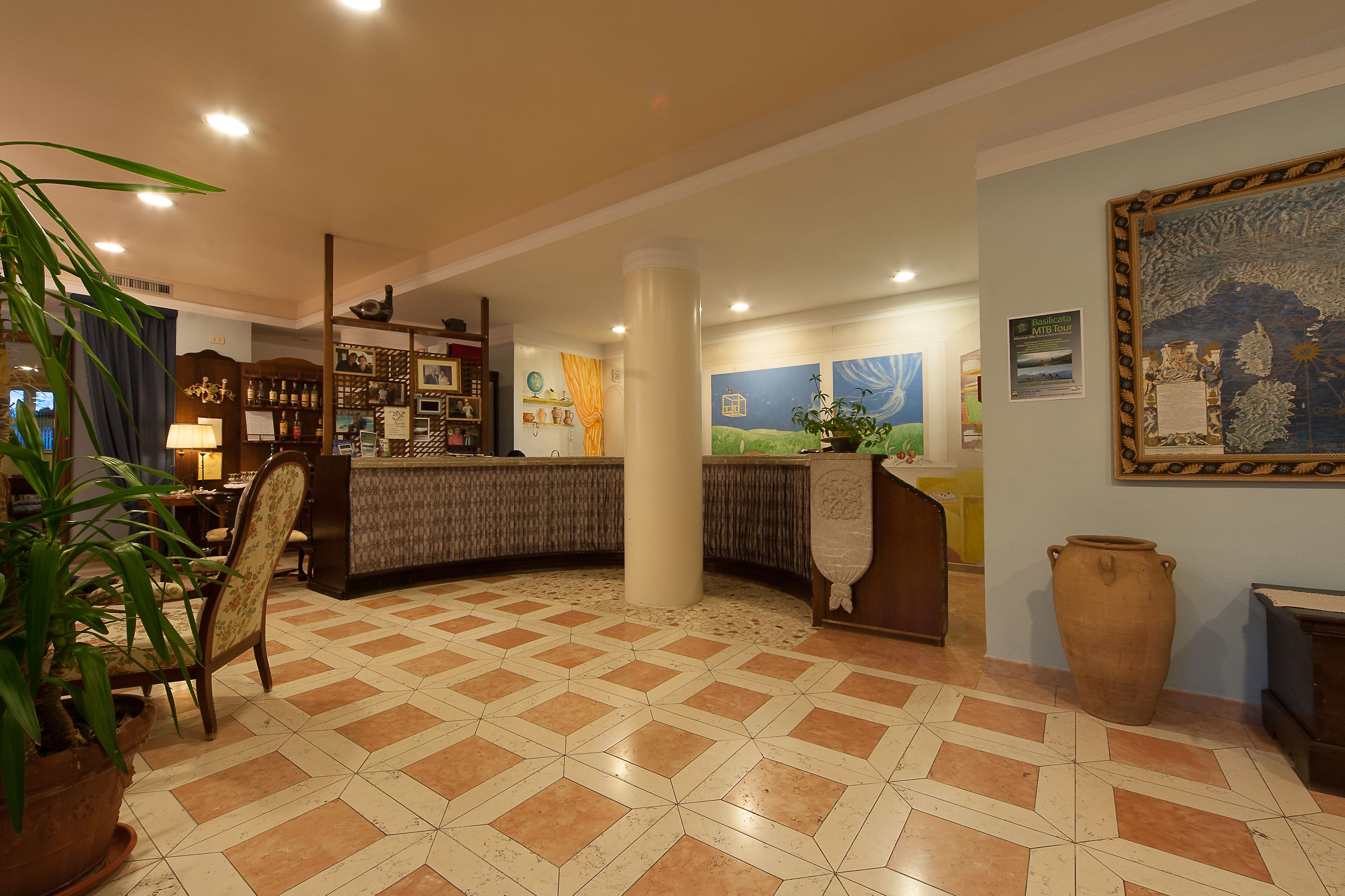 Un hall de hotel con mostrador de recepción, un gran jarrón y una planta en maceta.