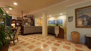 Un hall de hotel con mostrador de recepción, un gran jarrón y una planta en maceta.