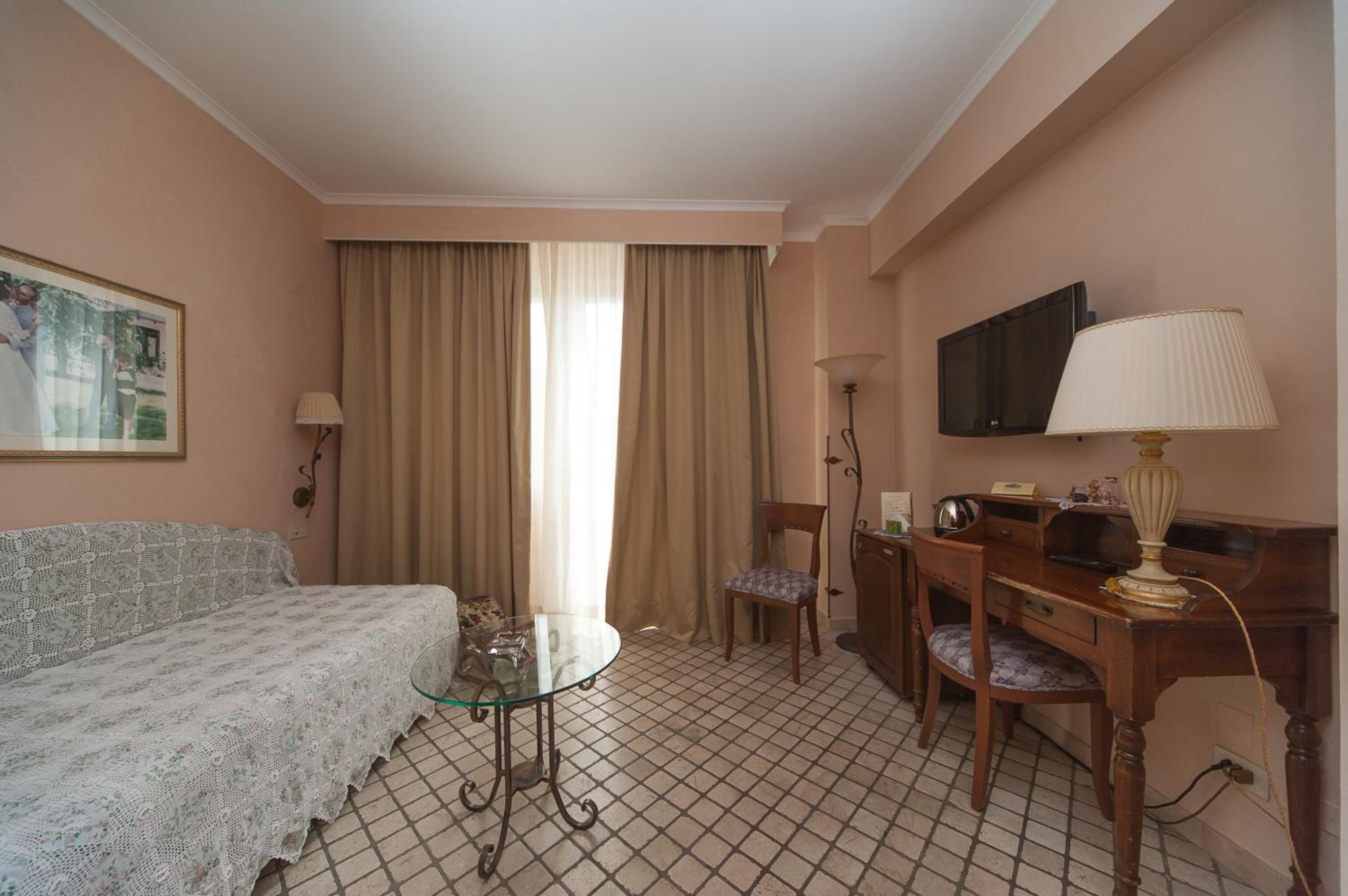 Une chambre d’hôtel avec un lit, un bureau avec une lampe, une télévision et une fenêtre avec des rideaux.