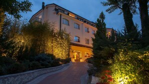 A multi-story hotel with a central entrance, surrounded by lush greenery and a stone pathway leading to the entrance. - La Primula (Potenza)