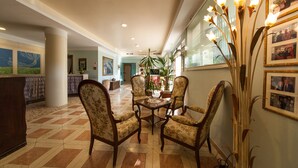 A lobby with a check-in counter, floral armchairs around a wooden table, and framed photos on the walls. - La Primula (Potenza)