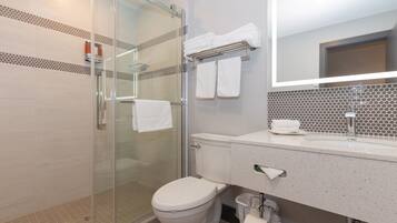 A modern bathroom with a glass shower enclosure, a toilet, a sink with a mirror, and a towel rack.