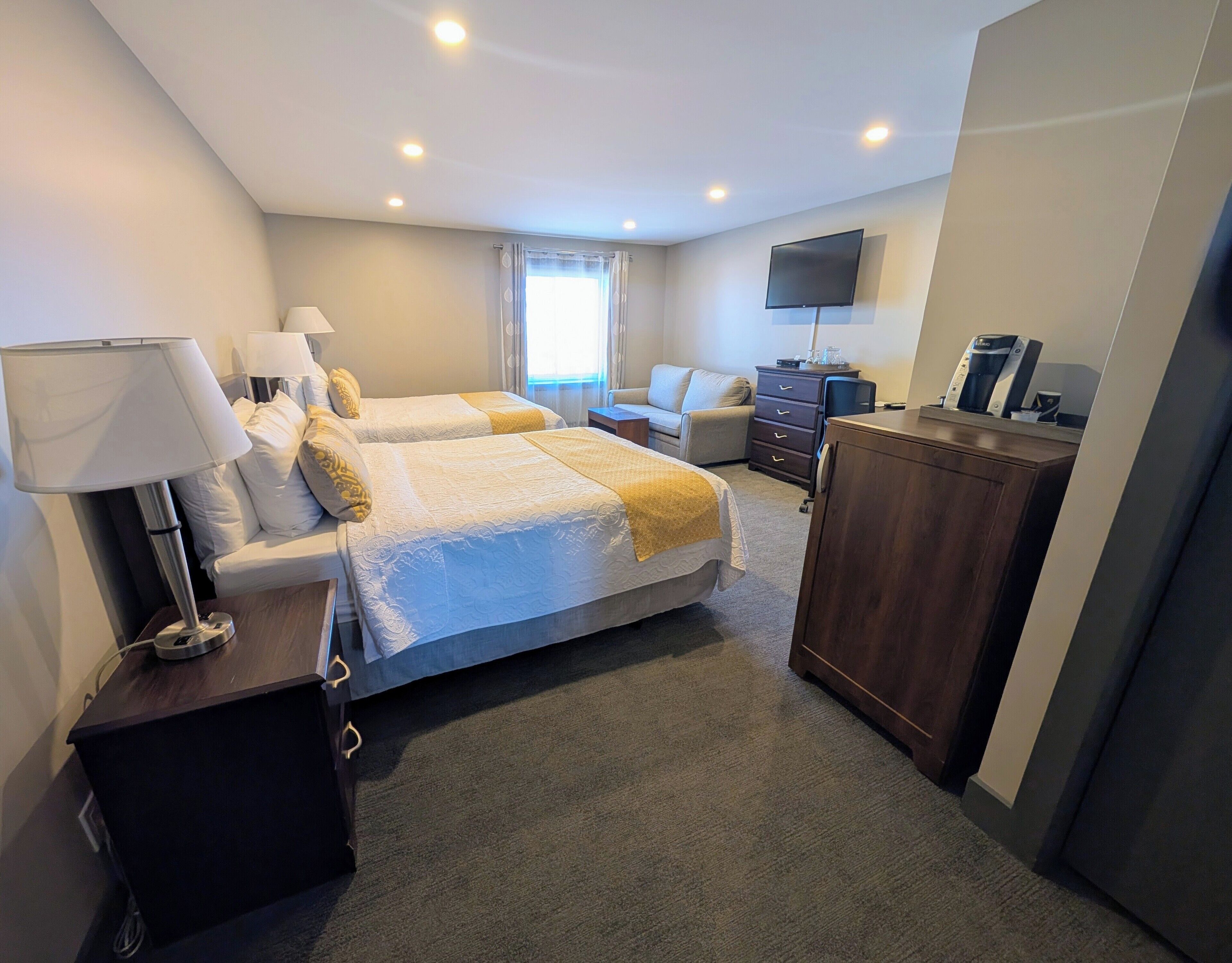 Habitación de hotel con dos camas, un televisor de pantalla plana, un aparador y un escritorio con lámpara.