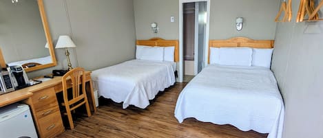 Une chambre d’hôtel avec deux lits, un bureau avec un ordinateur, une chaise, un miroir et un ventilateur de plafond.