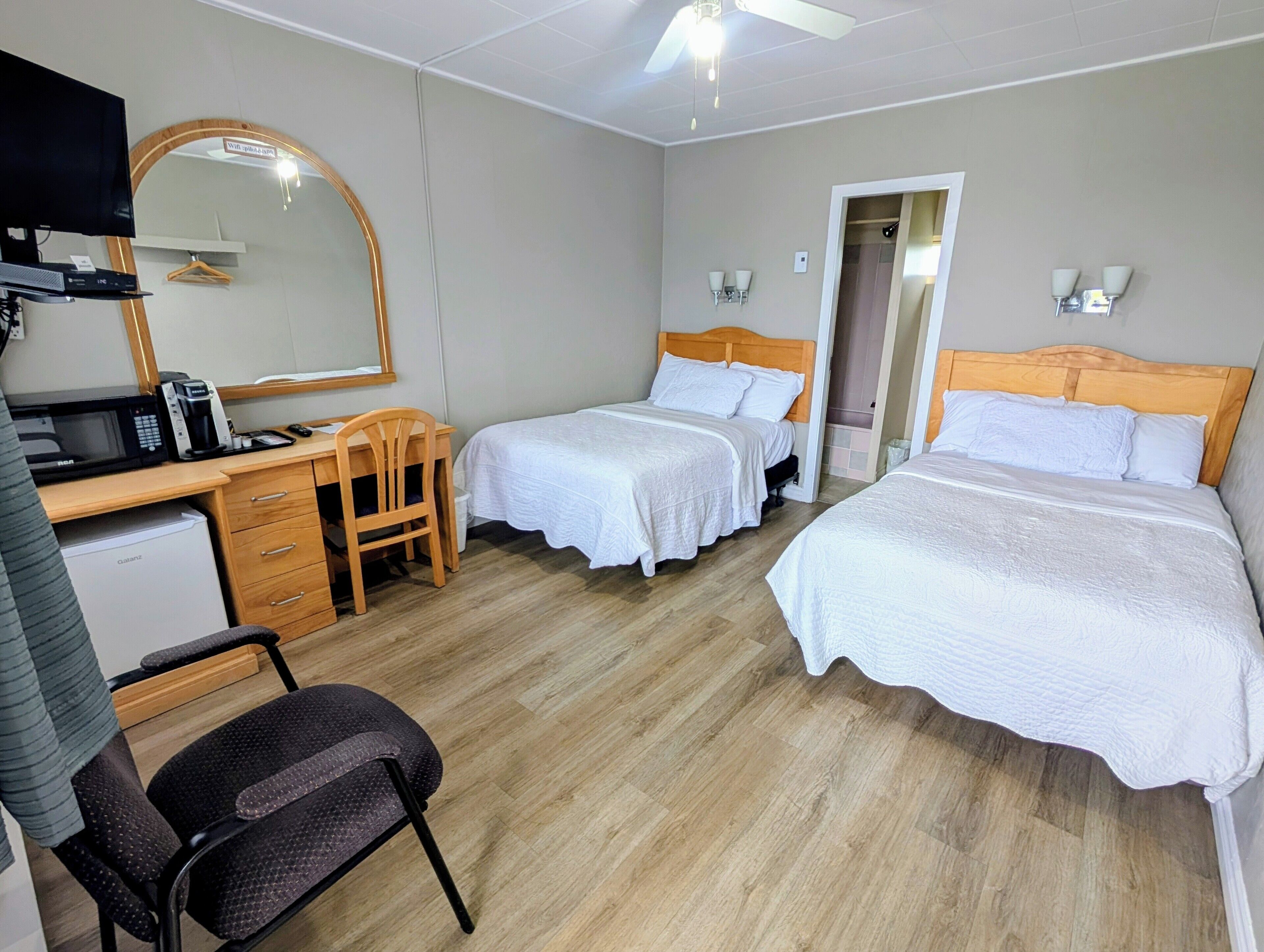 Ein Hotelzimmer mit zwei Betten, einem Schreibtisch mit Stuhl, einer Mikrowelle und einem Kühlschrank.