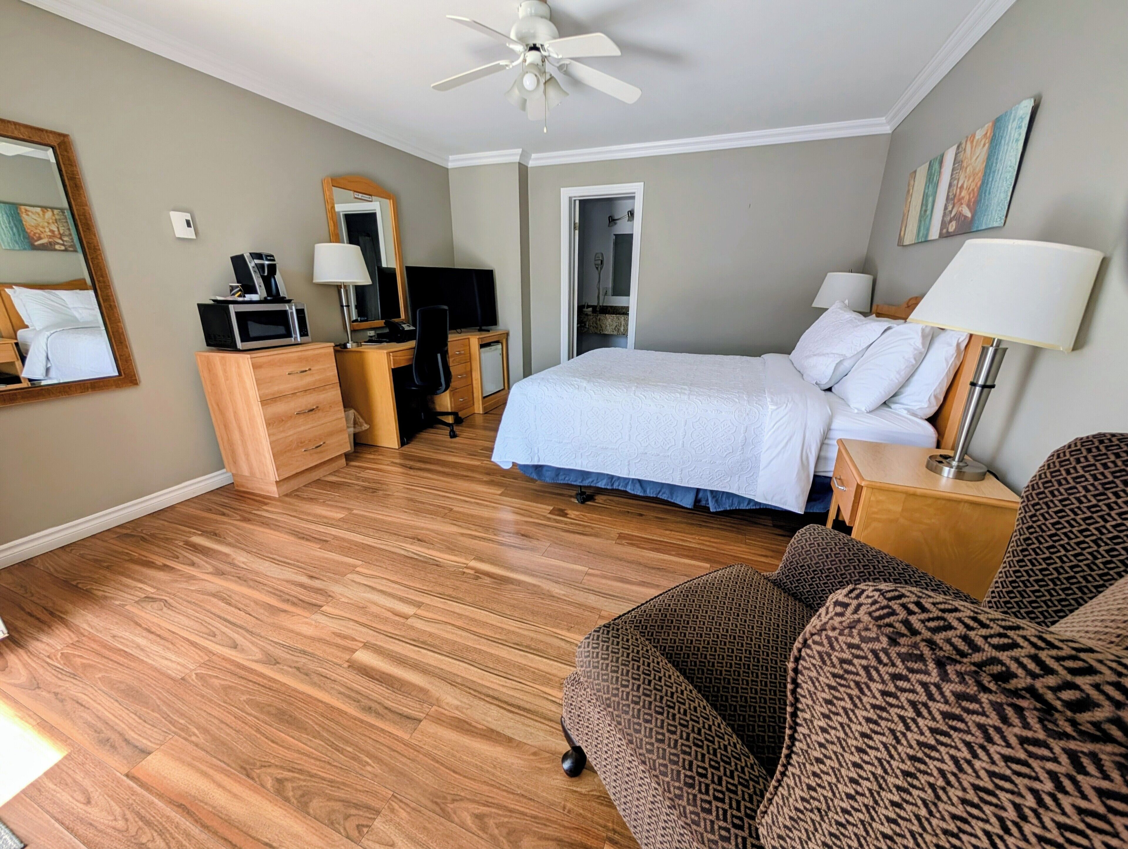 A hotel room with a bed, desk, chair, dresser, and a ceiling fan.