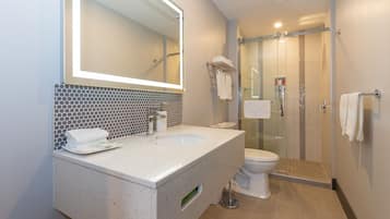 Un baño moderno con un espejo grande, un lavamanos y una ducha con mampara de vidrio.