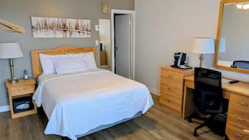 Een hotelkamer met een bed, een bureau, een stoel, een spiegel, een schilderij en een plafondventilator.