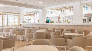 A modern cafe with round tables and chairs, a bar area, and a view of the street. - BLUESEA Don Jaime (Son Servera)