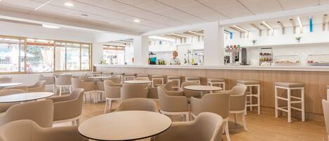 A modern cafe with round tables and chairs, a bar area, and large windows.
