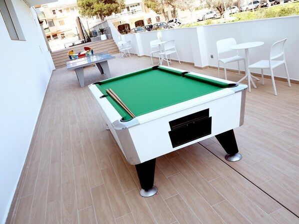 A pool table with a green felt surface, surrounded by white chairs and a glass table.