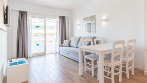 A modern living room with a sofa, dining table, and chairs. There is a sliding glass door leading to a balcony. - BLUESEA Don Jaime (Son Servera)