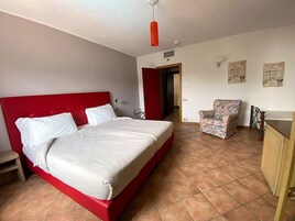 Un dormitorio con cama roja, almohadas blancas, una silla y un escritorio.