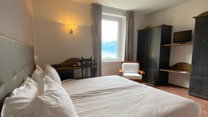 A hotel room with a large bed, a desk, a chair, a TV, and a wardrobe. - Albergo Lenno (Tremezzina)